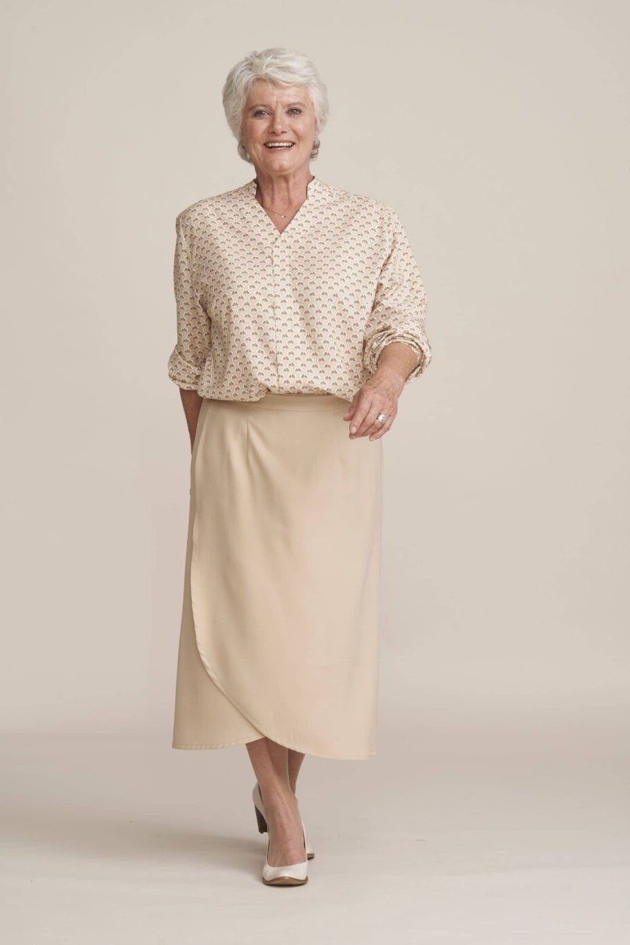 Woman over 50 in beige polka-dot blouse and cream wrap pencil skirt