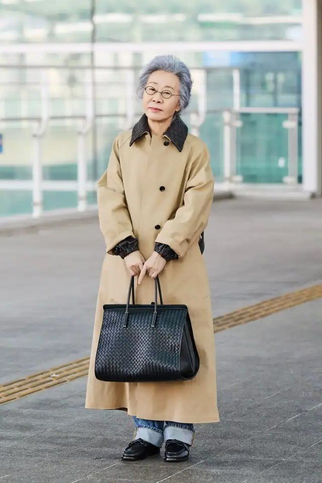 Woman over 50 in long camel coat, gray sweater and blue jeans