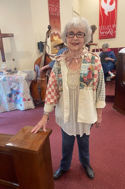 Older woman in colorful patchwork cardigan with dark jeans in church