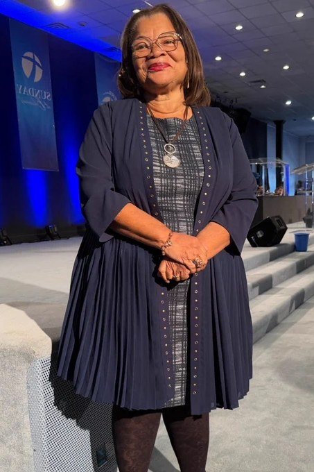 Older woman in navy pleated coat-dress with necklace