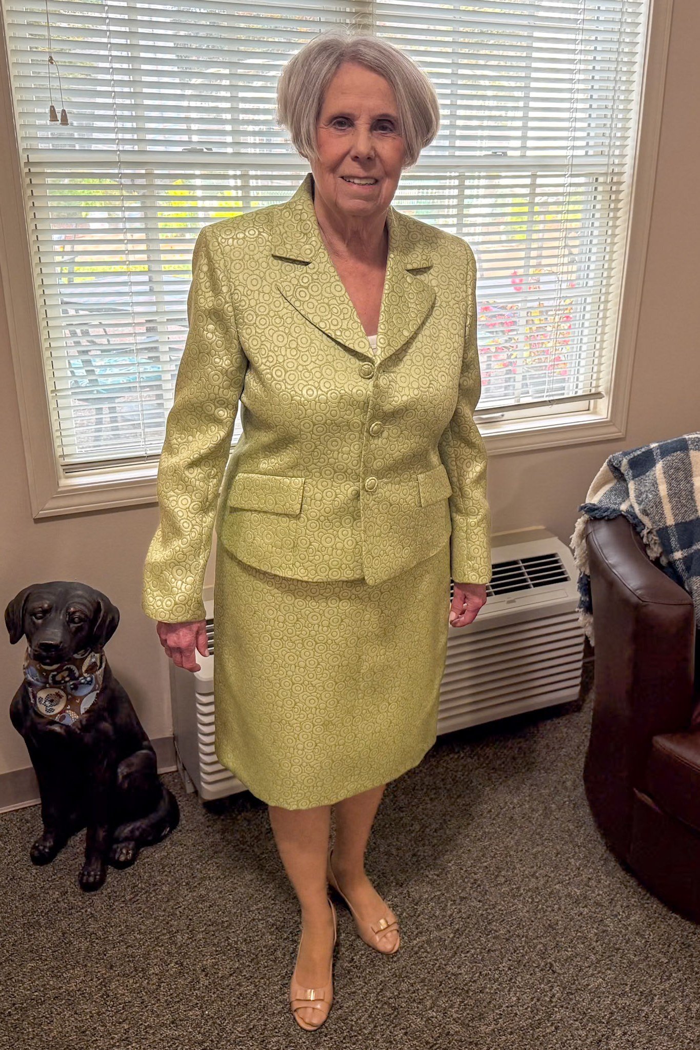 Older woman in gold brocade jacket and skirt suit indoors