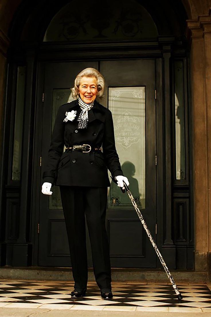 Older woman in black coat with white gloves and cane at church door