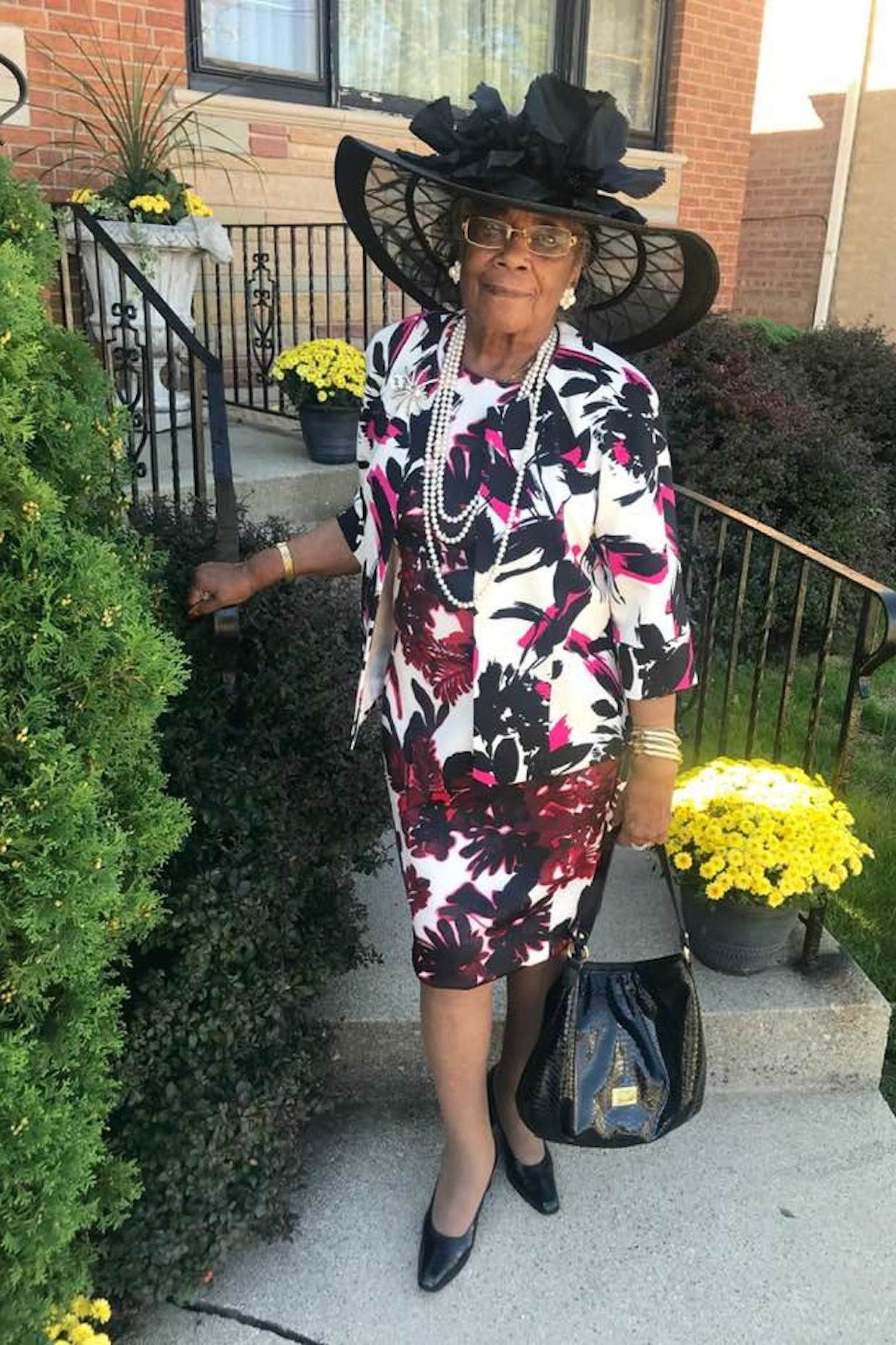 Older woman in floral dress with large patterned hat outdoors