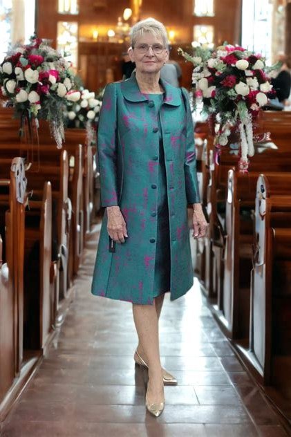 Older woman in teal floral coat-dress walking down church aisle