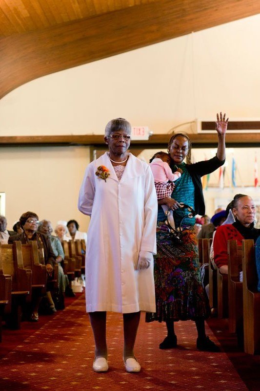 Older woman in white midi dress walking down church aisle