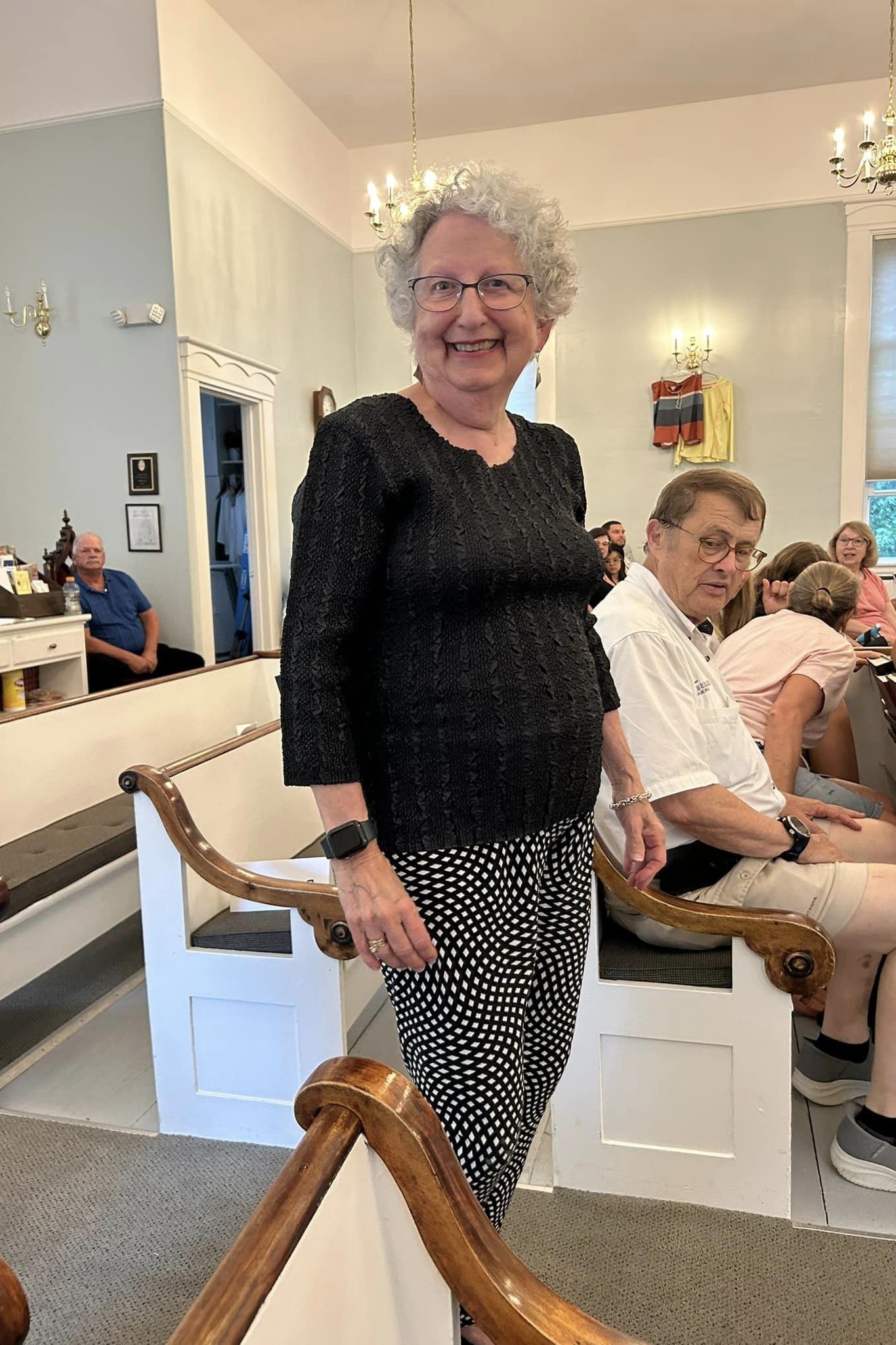 Older woman in black top with polka dot pants in church aisle