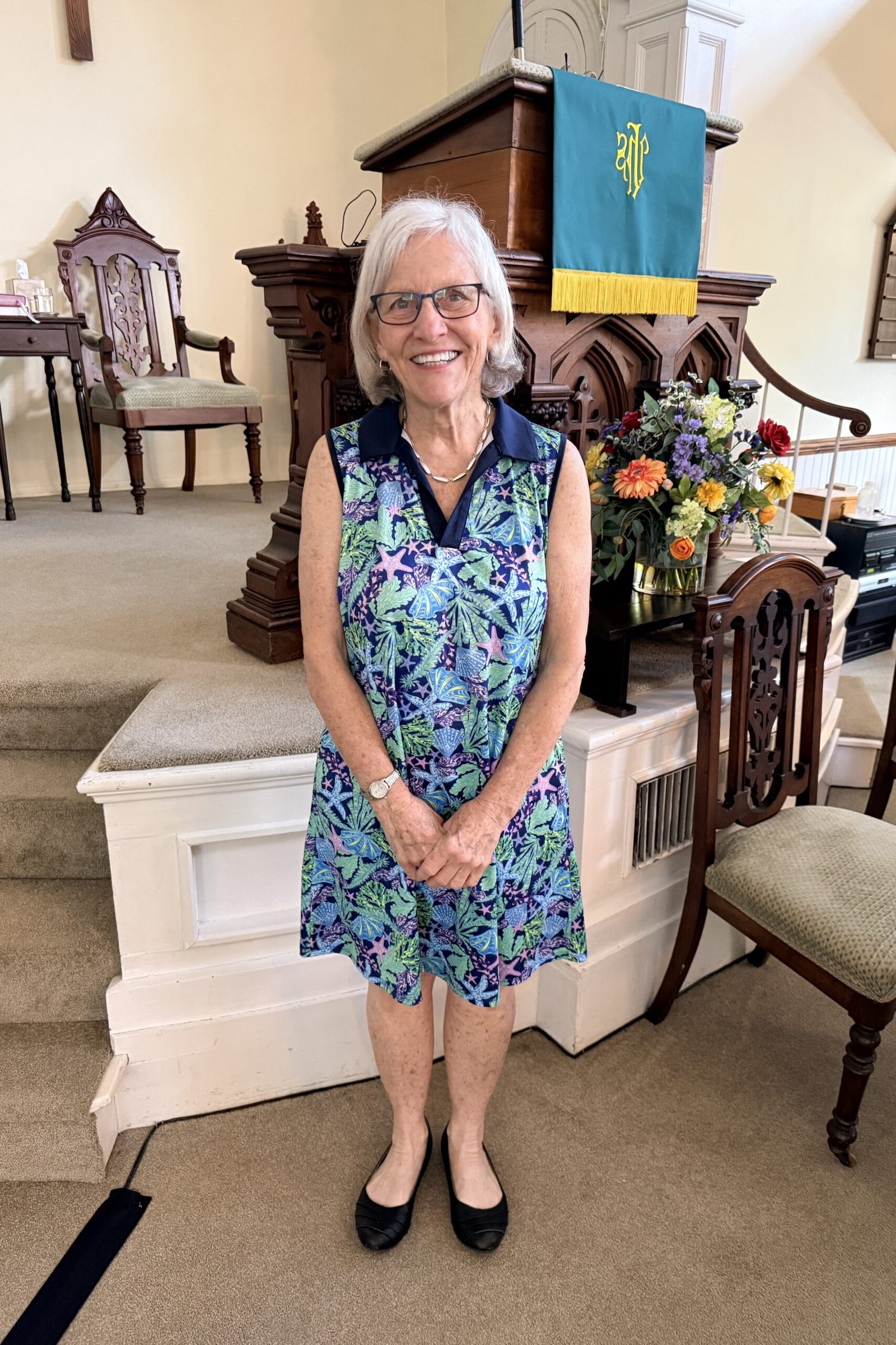 Older woman in blue floral sleeveless midi dress with black flats in church