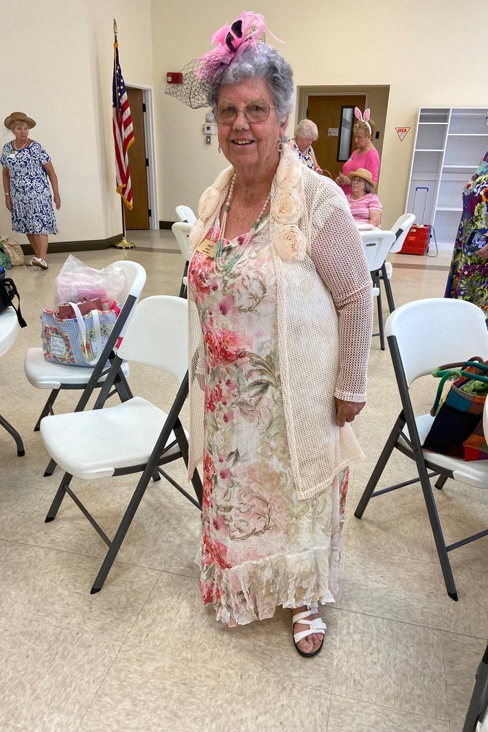 Older woman in cream floral lace midi dress with pink hat
