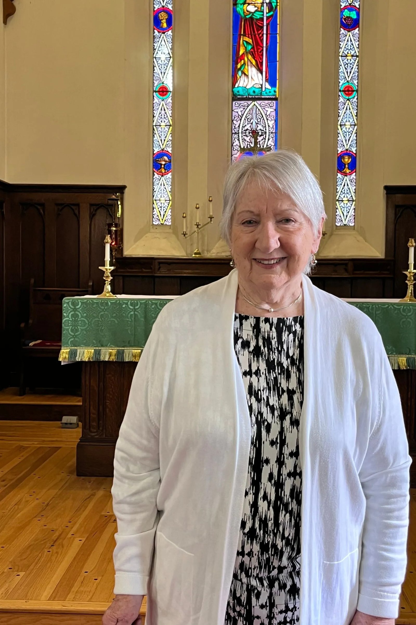 Older woman in white cardigan over black and white dress in church