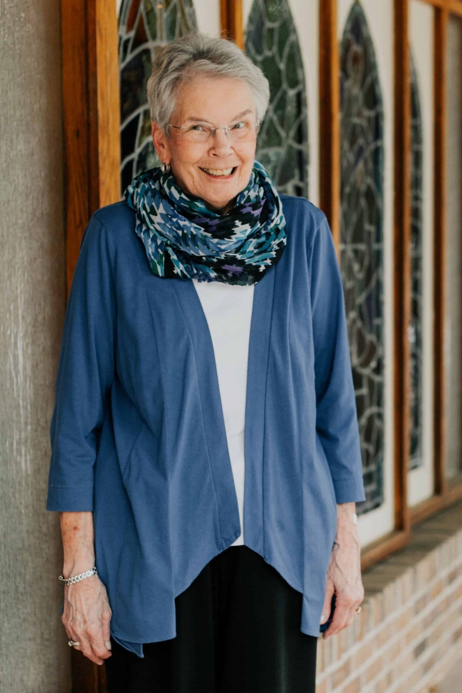 Older woman in blue cardigan with patterned scarf over white top