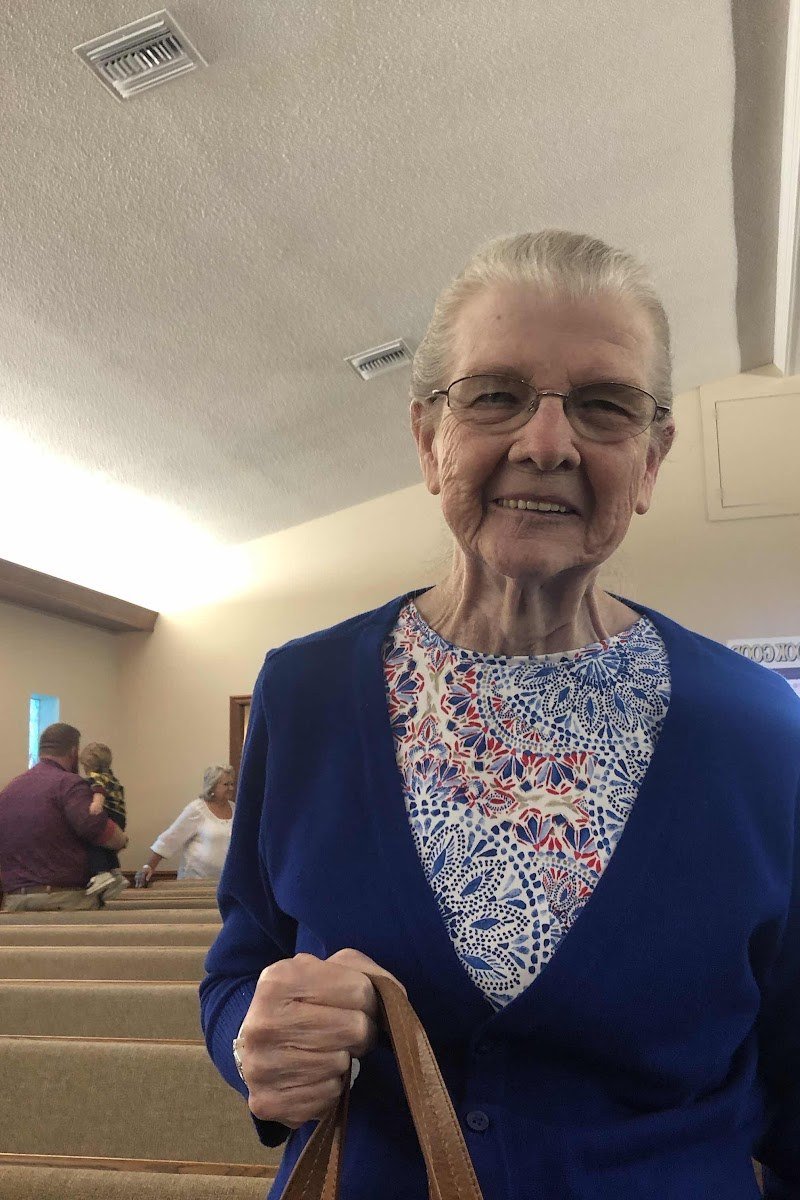 Older woman in navy cardigan over floral blouse in church aisle