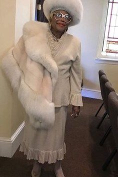 Older woman in cream fur-trim suit with white fur hat in church