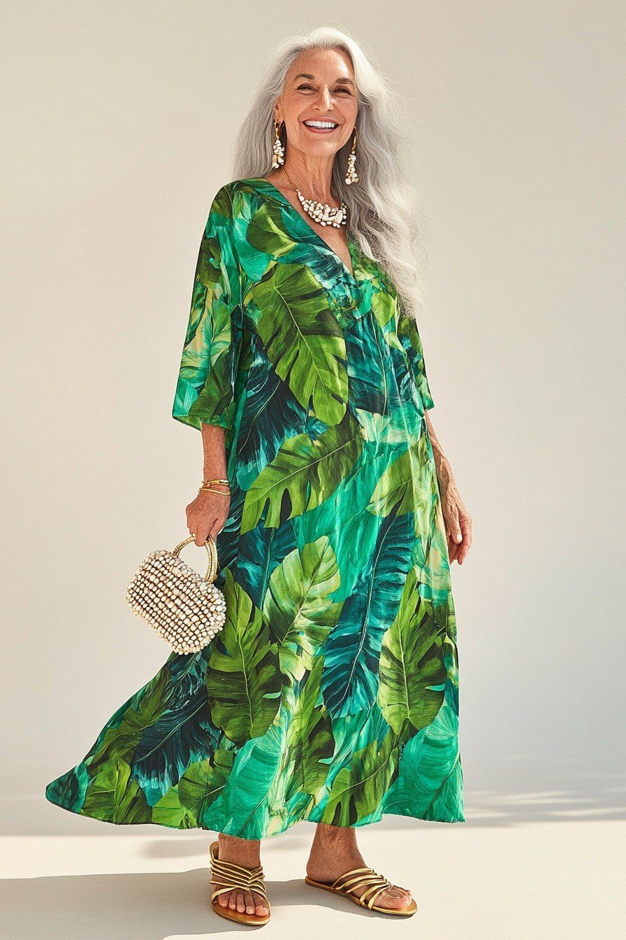 silver-haired woman in her 60s in a flowing emerald tropical-leaf print midi dress with strappy gold sandals and a small pearl clutch
