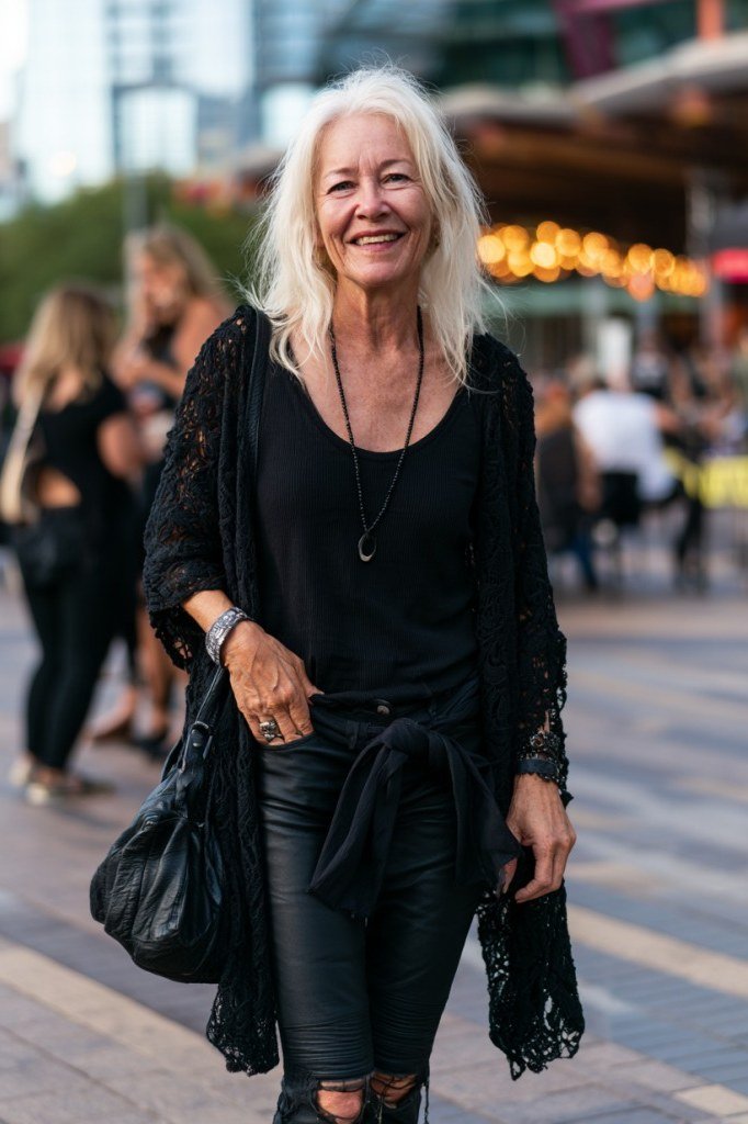 smiling silver-haired woman walking an outdoor venue in a black scoop-neck top and black leggings with a black lace cardigan tied around her waist