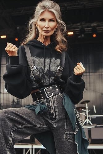 gray-haired woman dancing in front of a stage in a black graphic hoodie, baggy gray wide-leg jeans with a big belt and a flannel shirt tied at her waist