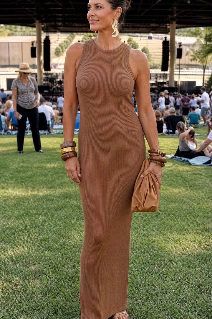woman in her 40s at an outdoor concert in a fitted brown ribbed knit maxi dress with a high neckline, stacked bracelets and a tan clutch