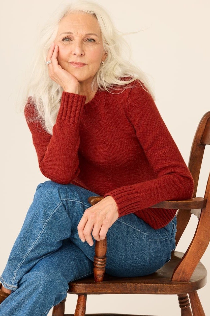 Rust red ribbed sweater with jeans, sitting on wooden chair - cozy casual outfit idea for women over 50
