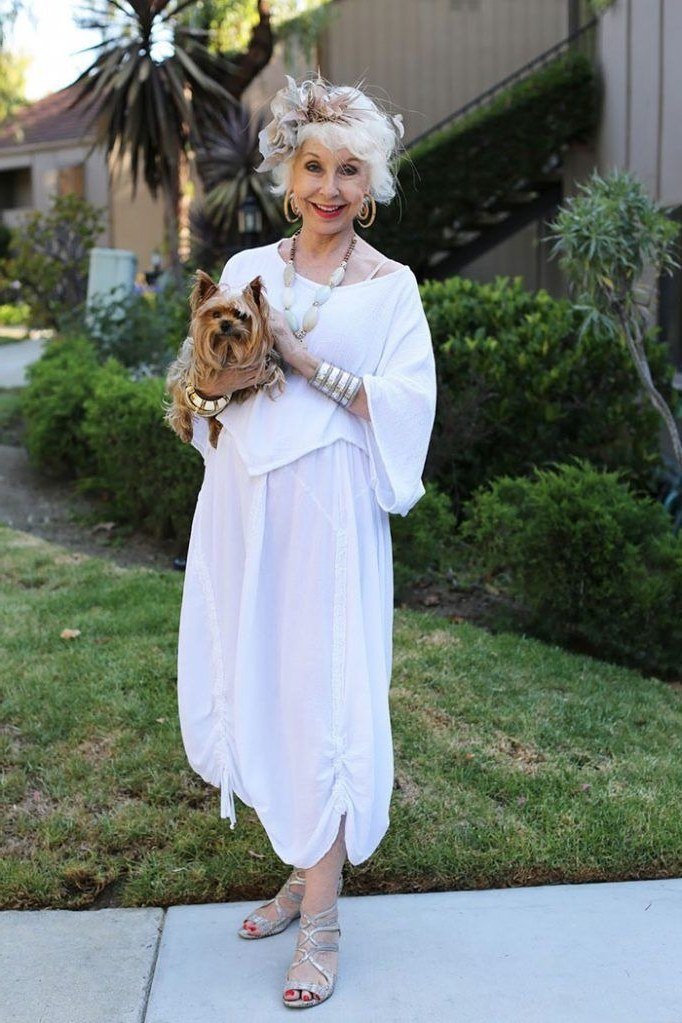 White off-shoulder maxi dress holding small dog on lawn