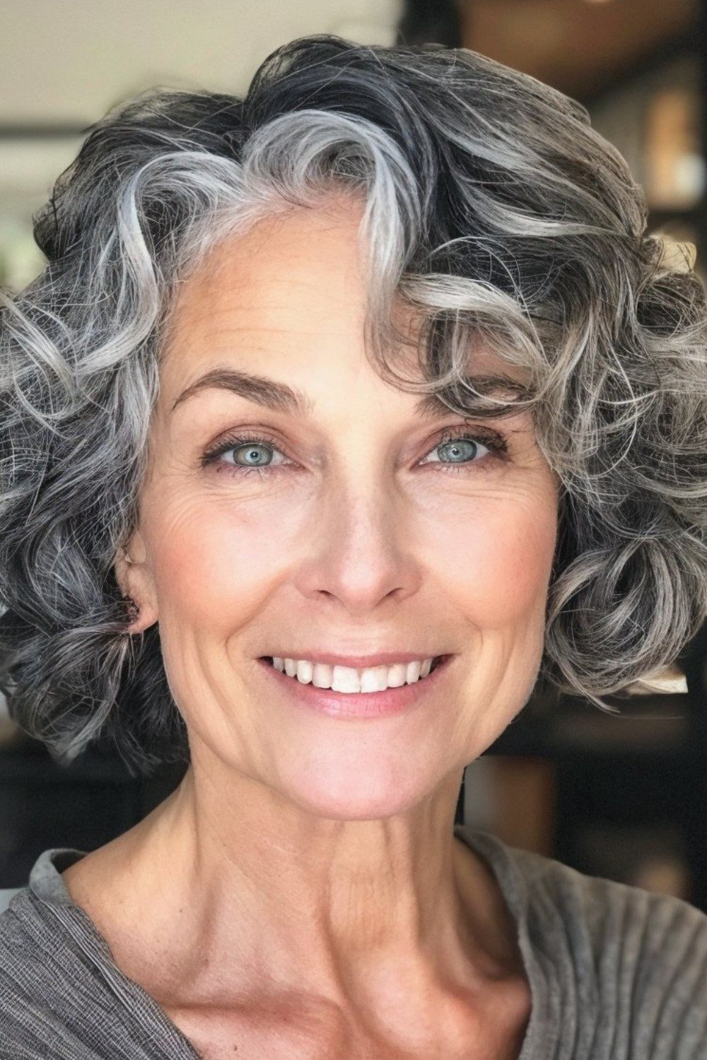 Salt-and-pepper curly bob haircut on a smiling older woman, curly hairstyles for women over 50
