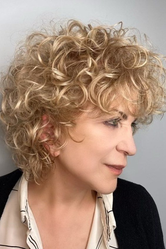 Voluminous champagne blonde curly bob on an older woman in a black blazer, curly hairstyles for women over 50
