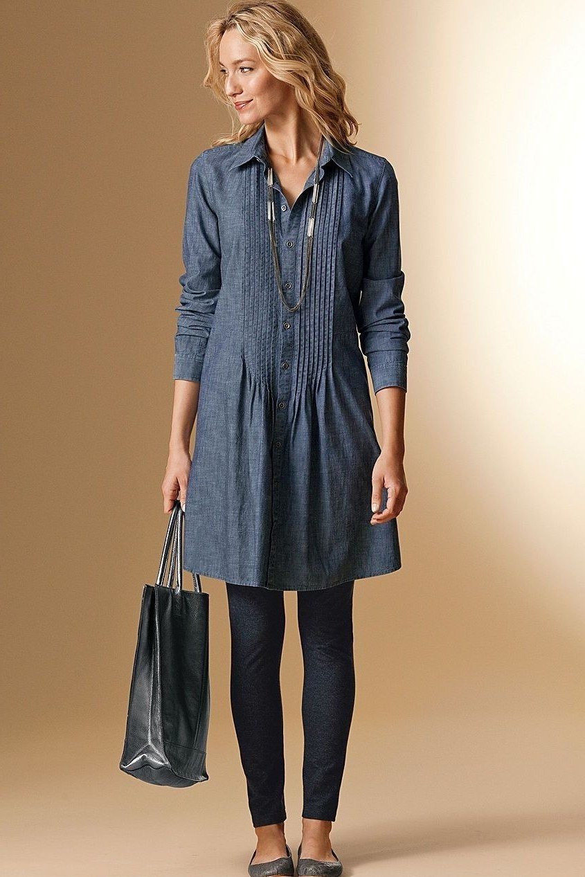 Woman in dark denim shirt dress over black leggings with black tote, studio, full front view - denim dresses for women over 60