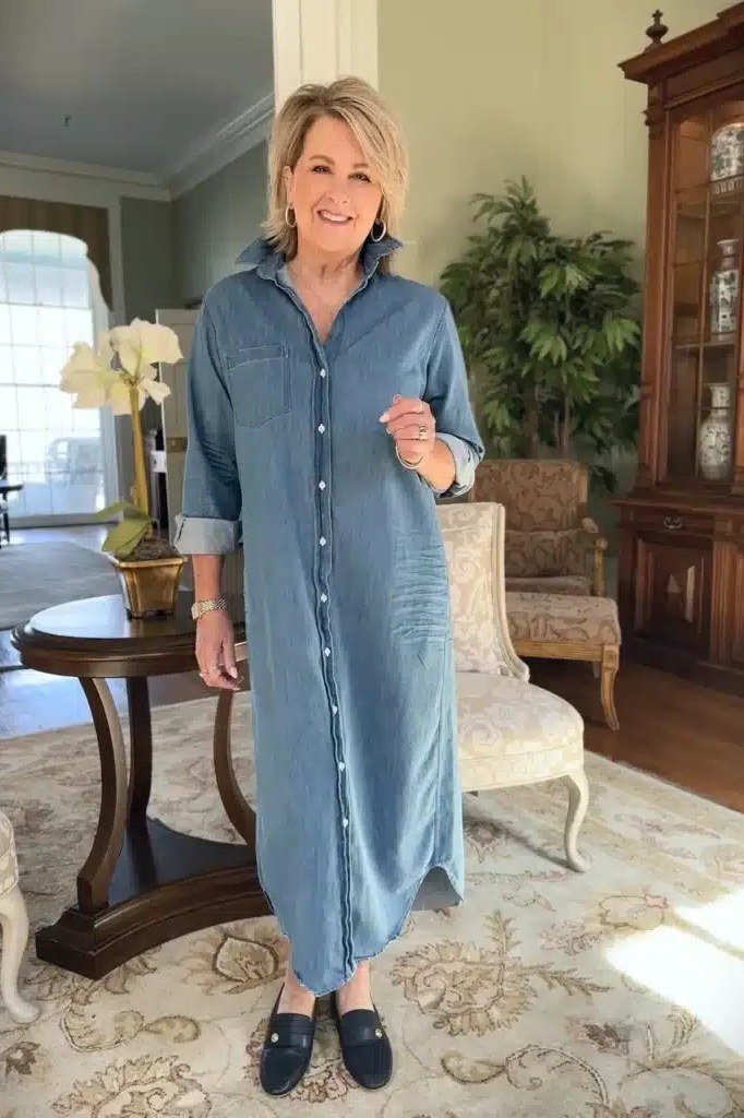 Blonde older woman in long dark denim shirt dress, elegant living room - denim dresses for women over 60