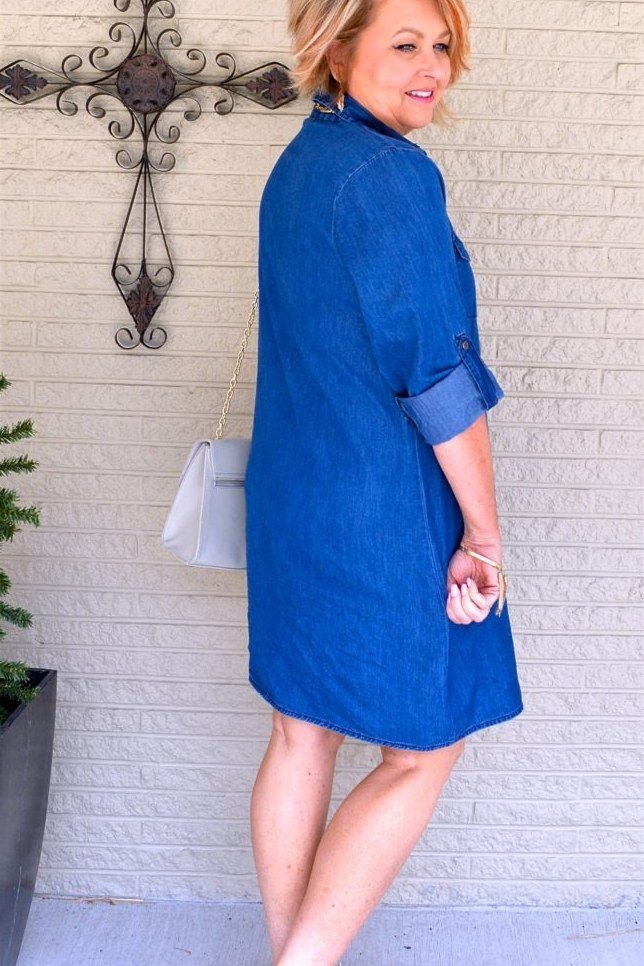 Blonde woman in denim shirt dress with white sneakers, three-quarter view by brick wall - denim dresses for women over 60