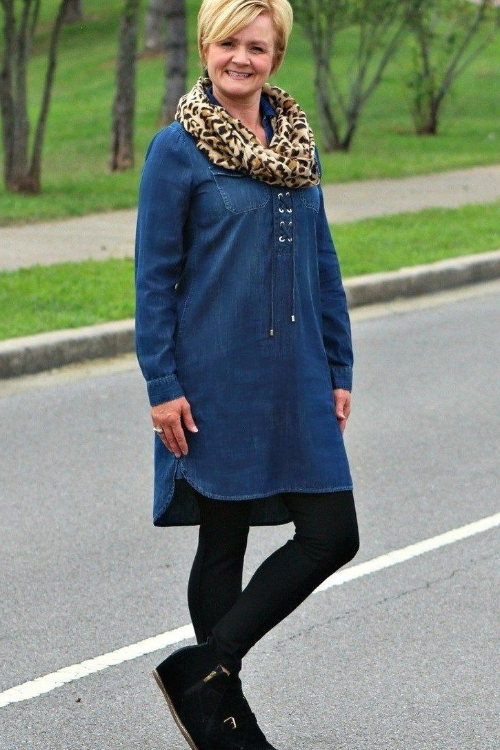 Blonde woman in dark denim shirt dress with black leggings, leopard scarf, black boots, outdoors by road - denim dresses for women over 60