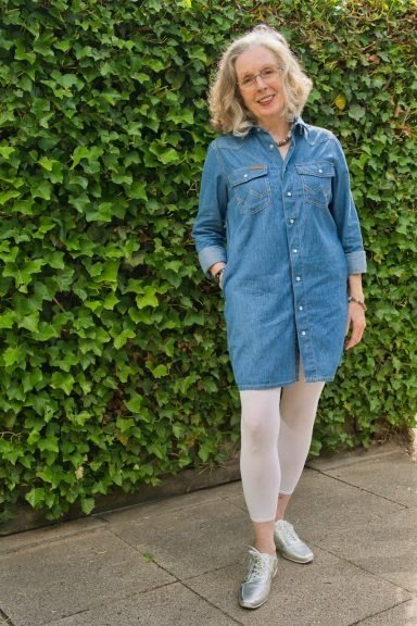 Blonde woman in denim shirt dress with white leggings and sneakers, ivy hedge - denim dresses for women over 60