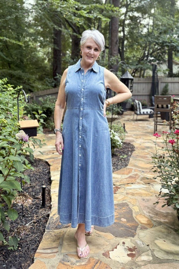 Older woman in sleeveless chambray maxi shirt dress, standing in garden - denim dresses for women over 60