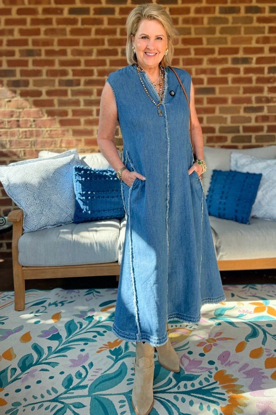Blonde woman in chambray maxi shirt dress, standing on porch with cushions - denim dresses for women over 60