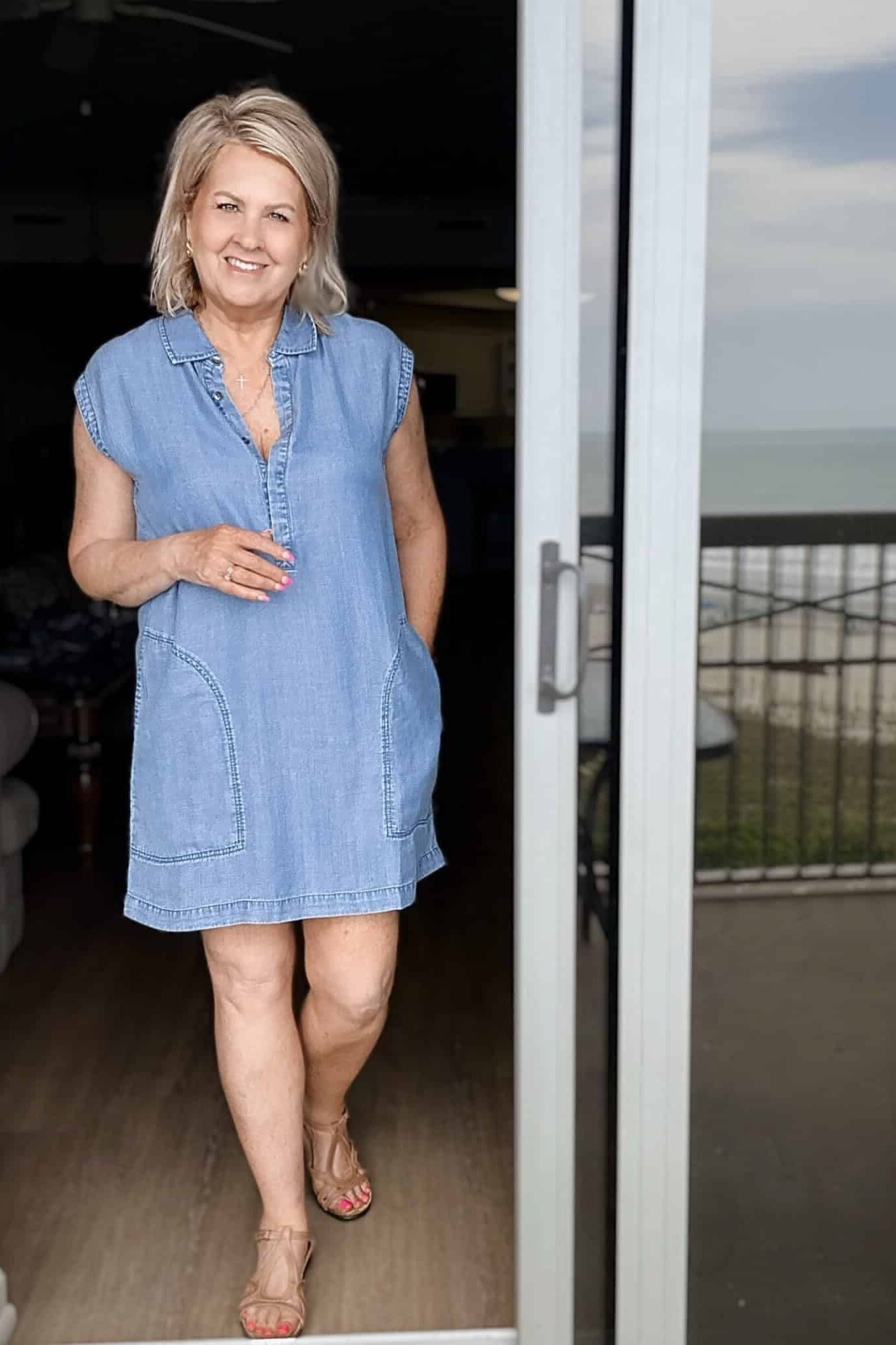 Blonde woman in light chambray shirt dress, walking through doorway - denim dresses for women over 60