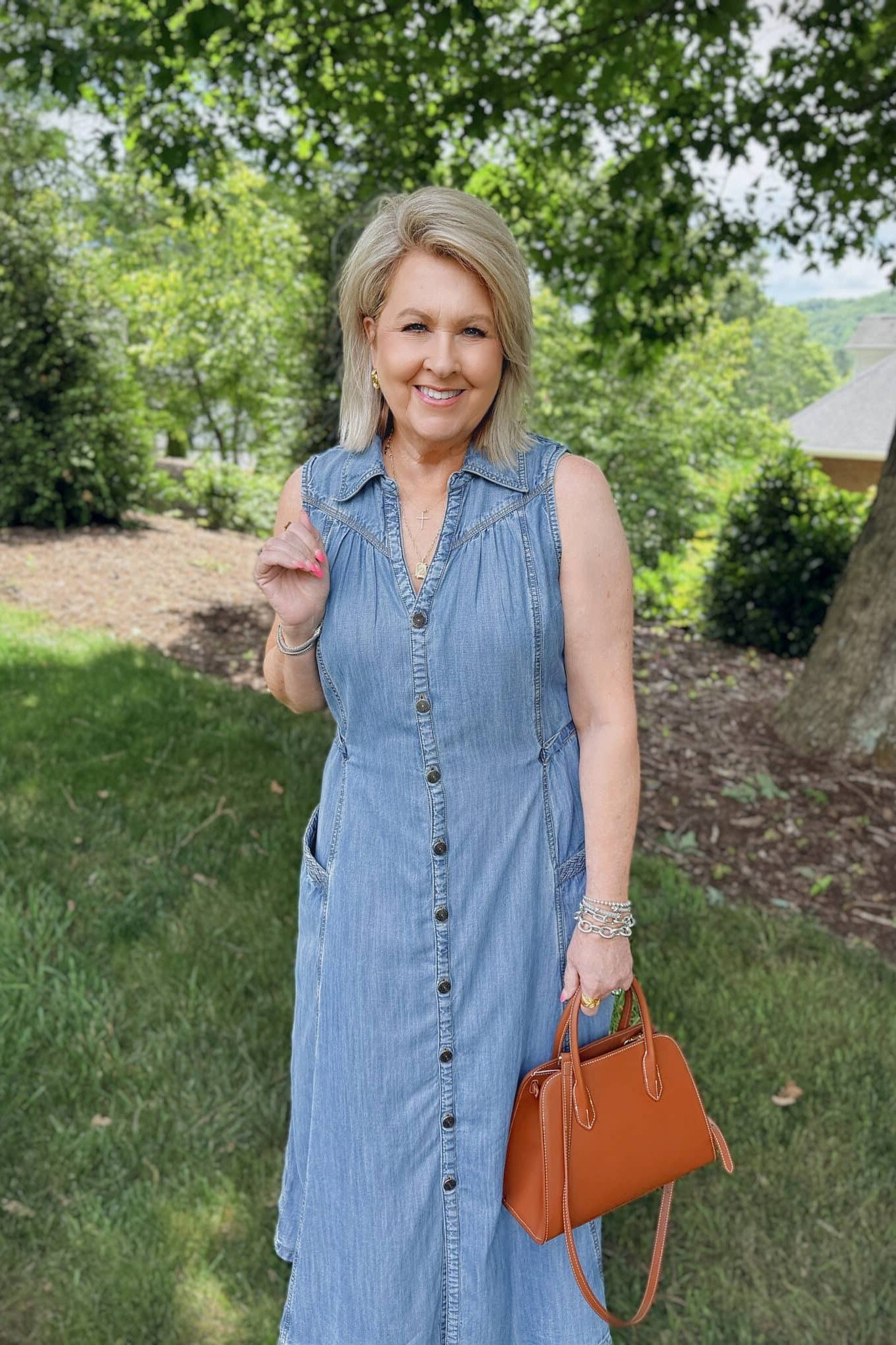 Blonde woman in sleeveless chambray maxi shirt dress with tan leather bag, garden - denim dresses for women over 60