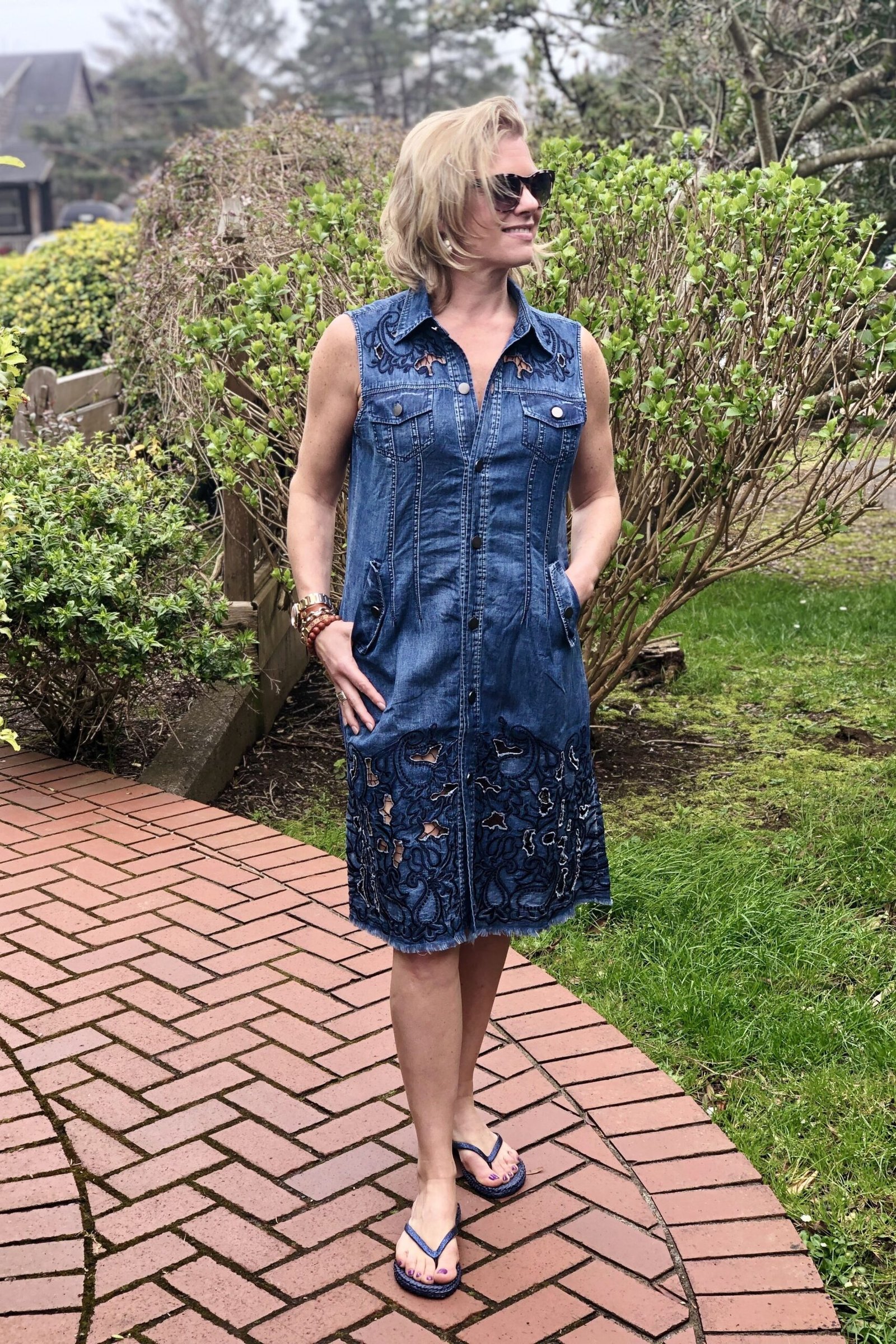 Woman in denim shirt dress with sunglasses, brick garden path - denim dresses for women over 60