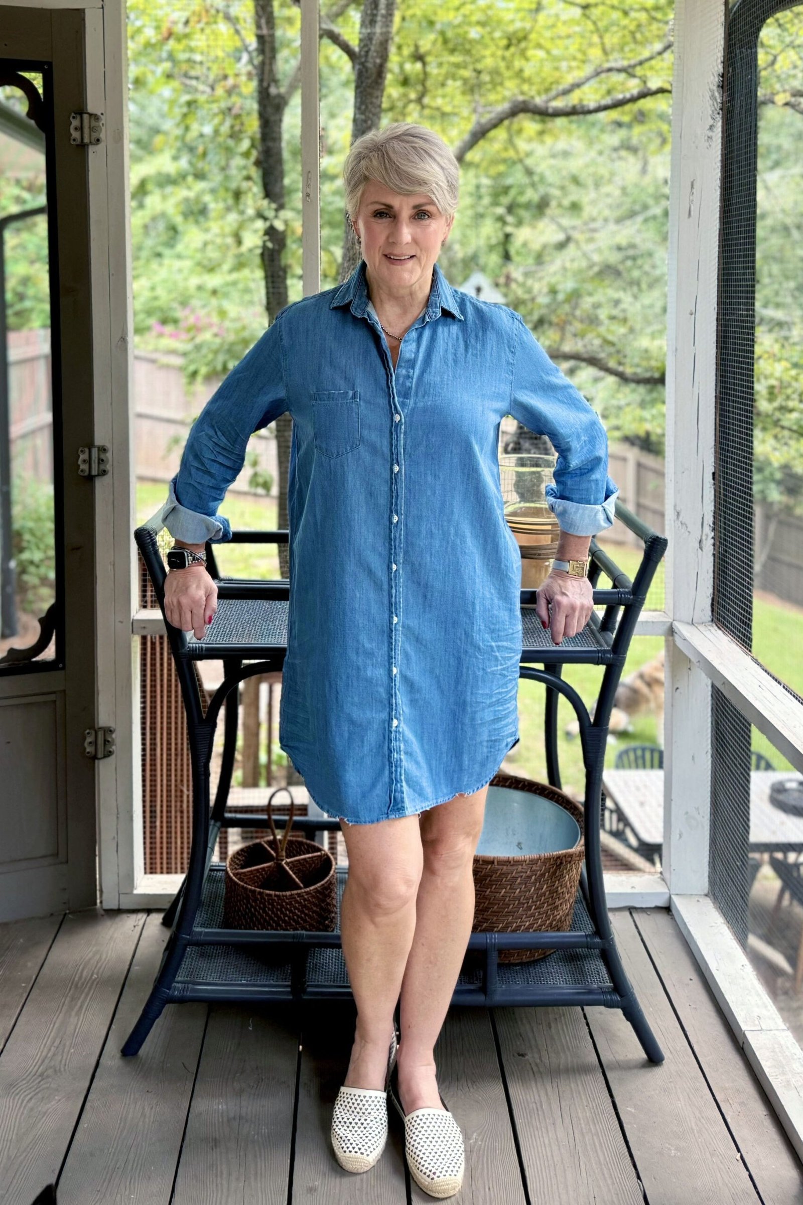 Older woman in denim shirt dress, screened porch with wicker chair - denim dresses for women over 60