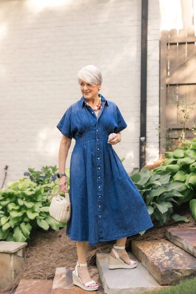 Older woman in dark denim midi shirt dress with small bag, garden - denim dresses for women over 60
