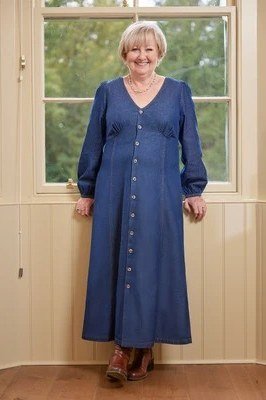 Older woman in dark denim button-front maxi dress, by bright window - denim dresses for women over 60