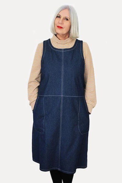 White-haired woman in dark denim pinafore dress over beige long-sleeve top, studio - denim dresses for women over 60