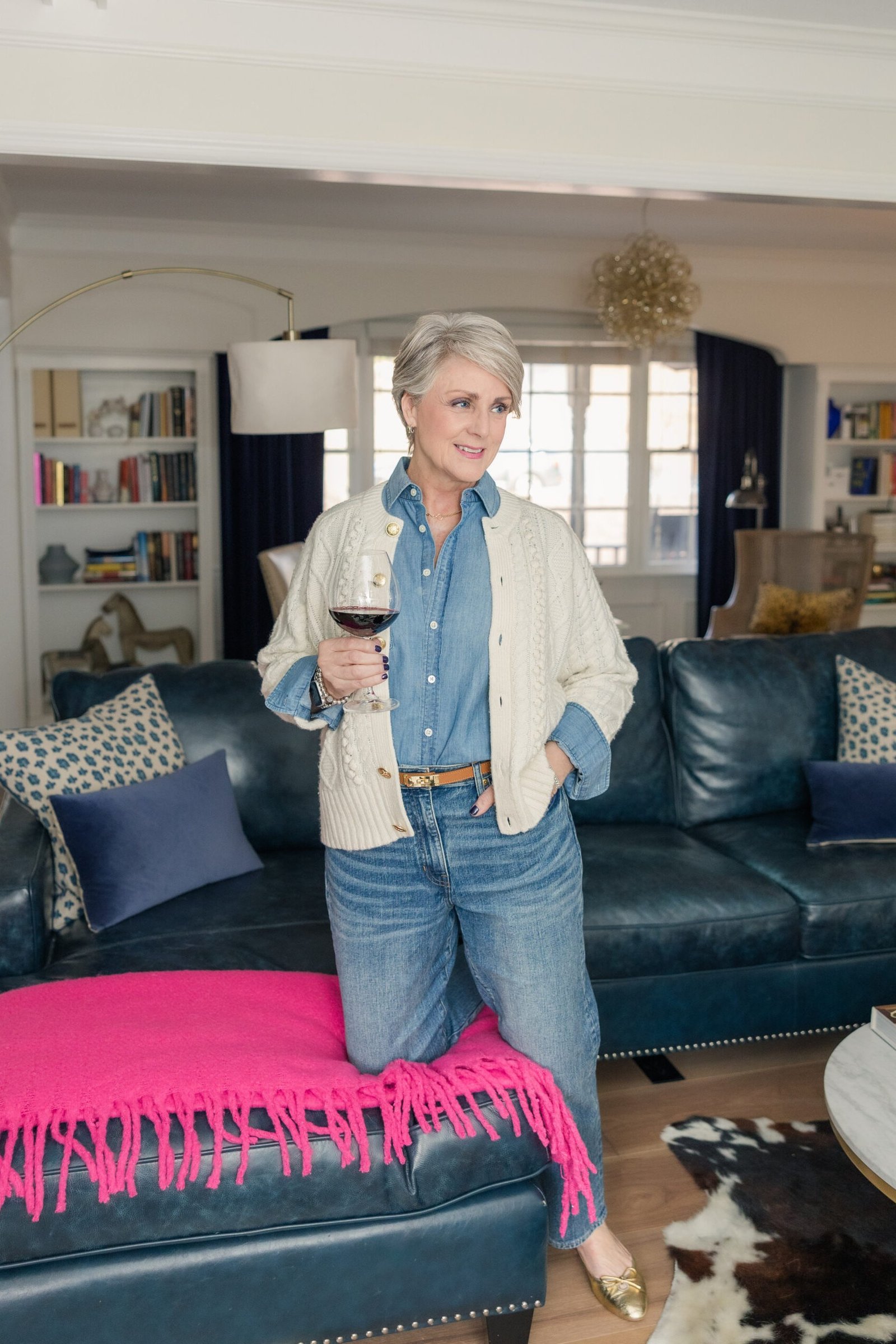 Cream cable-knit cardigan, chambray shirt, medium jeans, wine glass, living room - denim outfit idea for women over 50