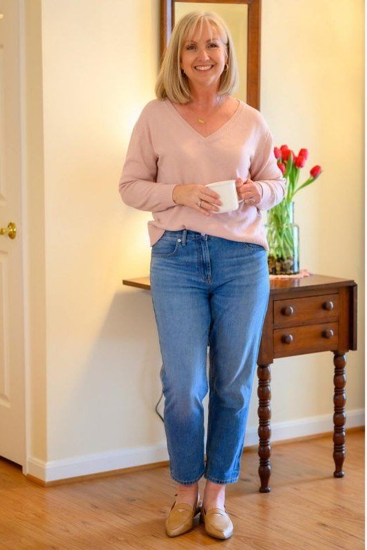 Pink sweater, medium jeans, holding mug - denim outfit idea for women over 50