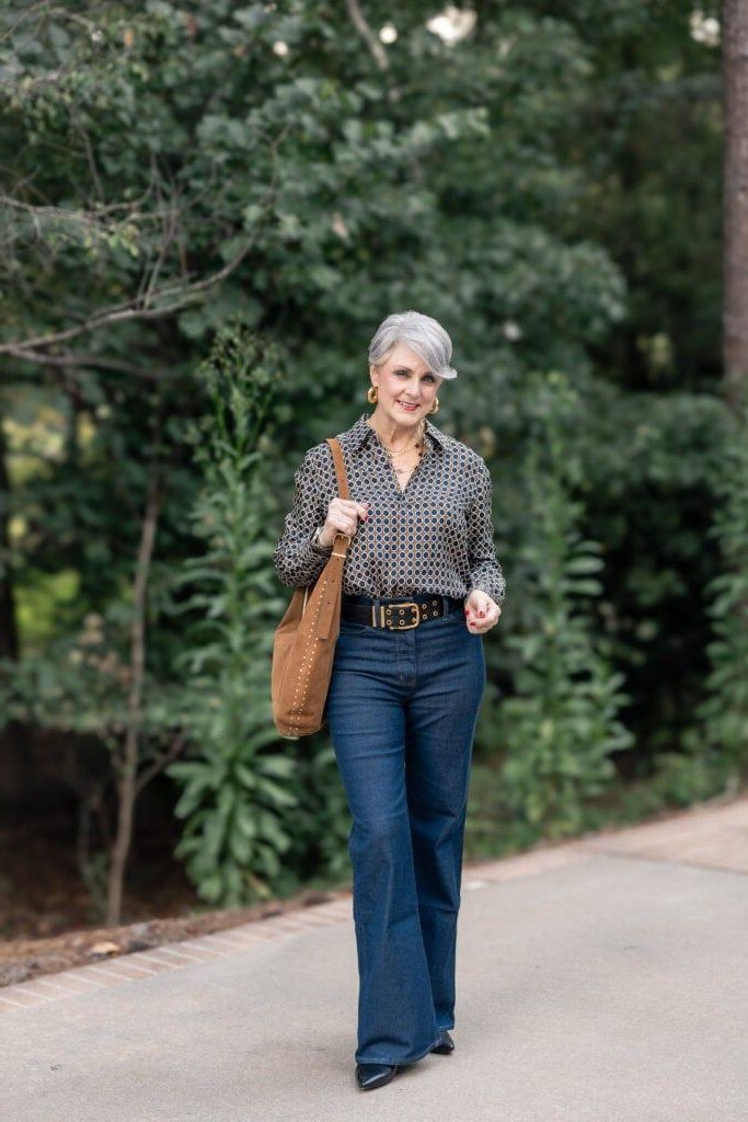 Patterned top, dark flared jeans, gray hair, outdoors - denim outfit idea for women over 50