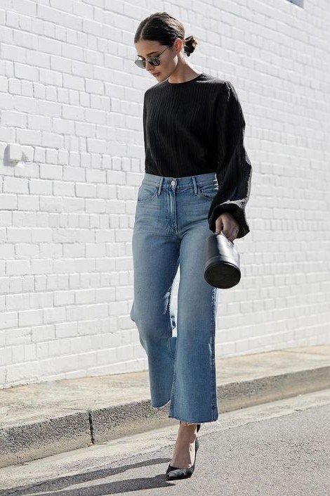 Black top, light wide-leg jeans, white wall - denim outfit idea for women over 50