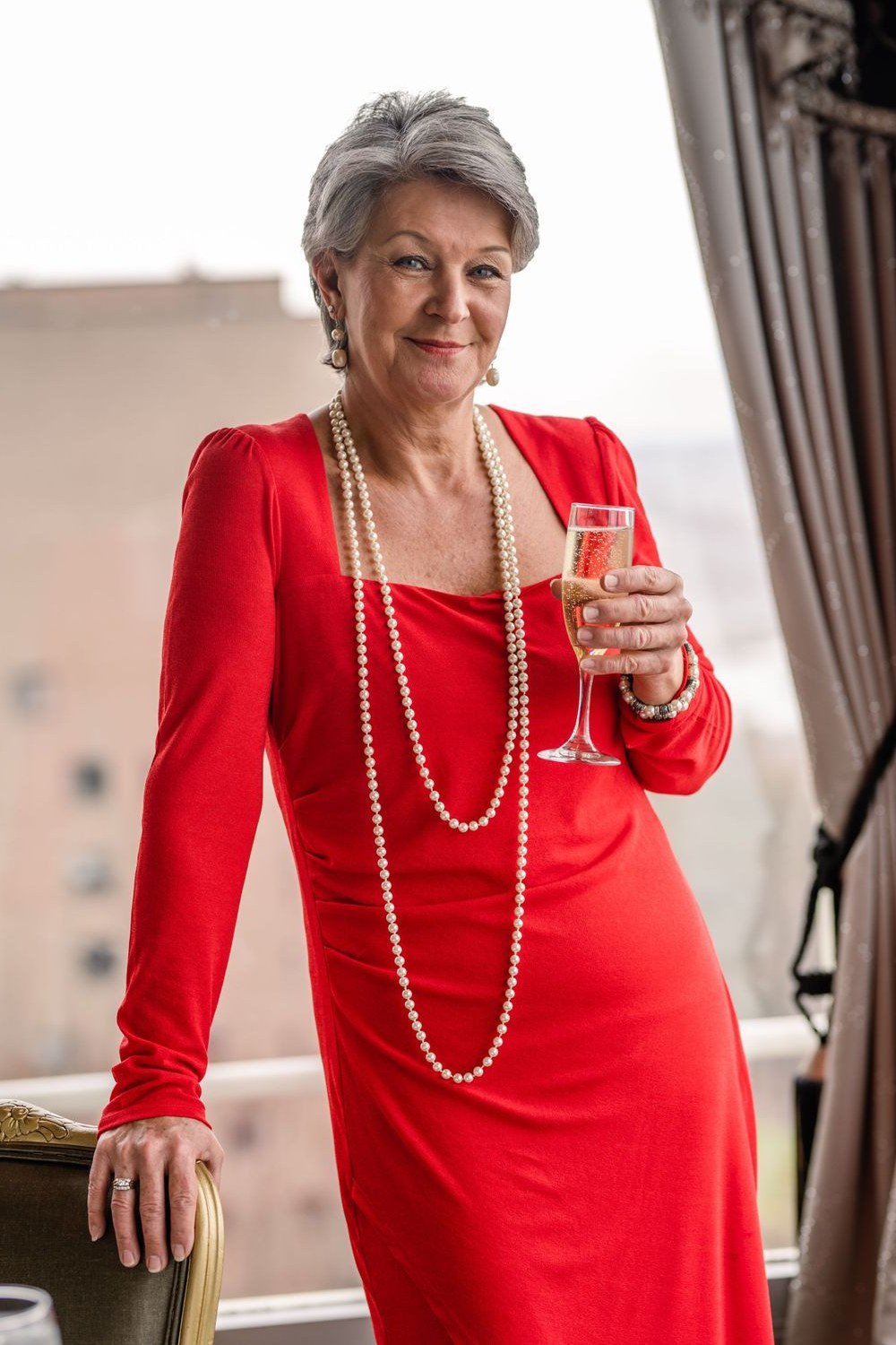 Red long-sleeve dress with pearls holding champagne for older women