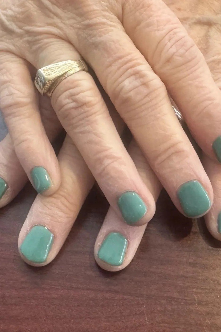 Sage green short nails on mature hands of a woman over 60