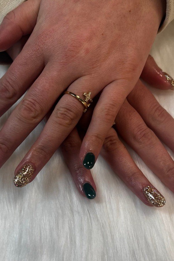 Dark green nails with gold glitter on mature hands of a woman over 60