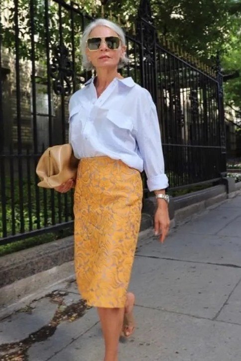 Elegant work outfit for women over 50: white blouse, yellow floral midi skirt, sunglasses, walking