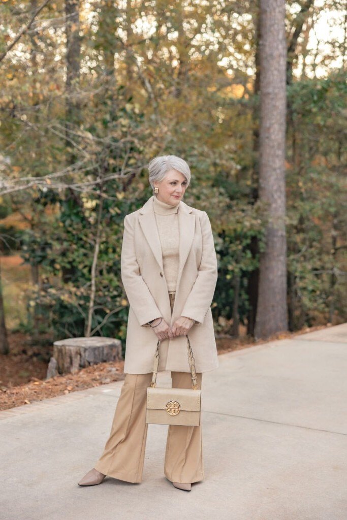 Elegant work outfit for women over 50: beige blazer, tan flared trousers, beige bag, autumn path