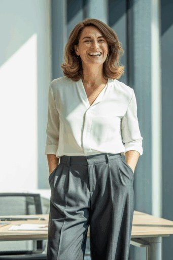 Elegant work outfit for women over 50: white blouse, grey wide-leg trousers, office desk