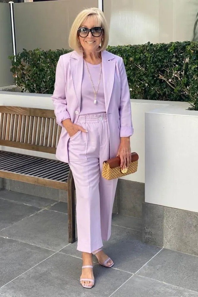 Elegant work outfit for women over 50: lavender suit, white top, woven clutch, bench