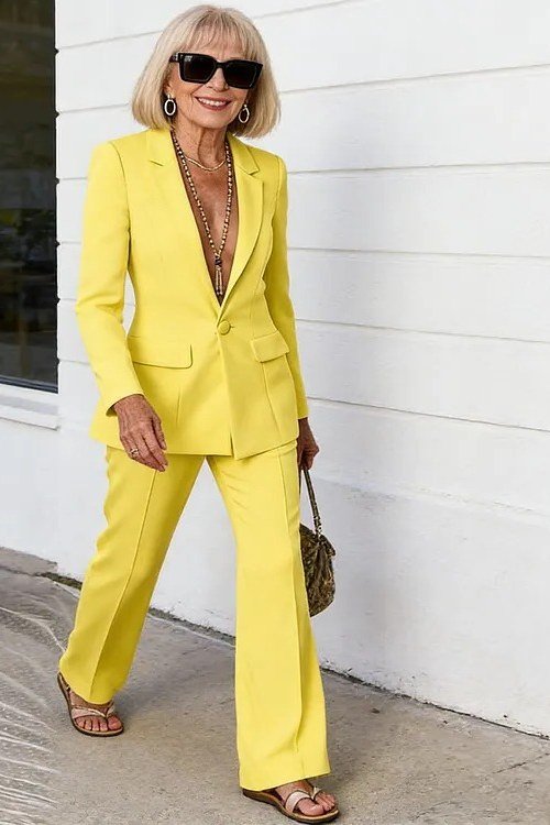Elegant work outfit for women over 50: bright yellow suit, woven bag, white wall